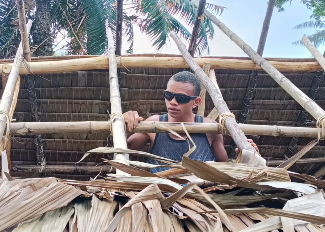 Photo of David Nalo’s son working on traditional thatched-roof building
